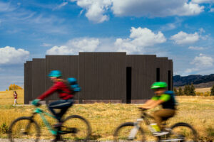 Two blurry bikers riding past a black, geometric public art display.